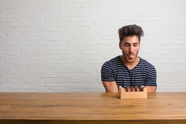 Homem considerável e natural novo que senta-se em uma expressão da tabela da confiança e da emoção, do divertimento e amigável, mostrando a língua como um sinal do jogo ou do divertimento. comendo rosquinhas de chocolate. Foto Premium