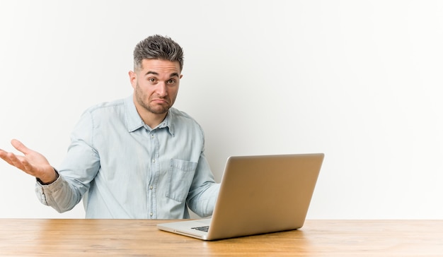 Homem considerável novo que trabalha com seu portátil que duvida e que shrugging ombros no gesto de questão. Foto Premium