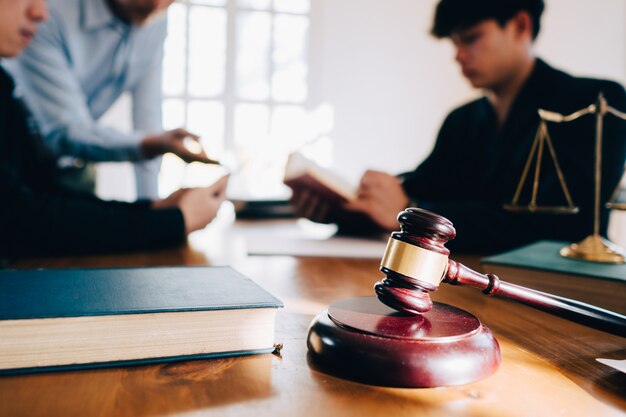 Homem de negócio e equipe e advogados que discutem papéis do contrato com a escala de bronze na mesa de madeira no escritório. lei, serviços jurídicos, conselhos, conceito de justiça. Foto Premium