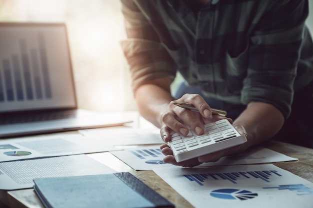 Homem de negócio que guarda a pena com utilização da calculadora para rever o anuário do balanço patrimonial com utilização do laptop ao orçamento calculador. auditar e verificar a integridade antes do conceito de investimento. Foto Premium