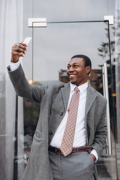 Homem de negócios americano africano no clássico terno cinza segurando um smartphone e fazer selfie. Foto Premium