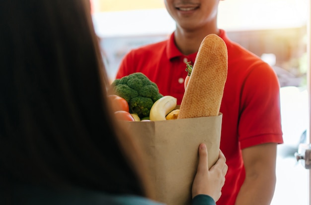 Homem de serviço de entrega de comida inteligente em uniforme vermelho, sorrindo e enviando alimentos frescos Foto Premium
