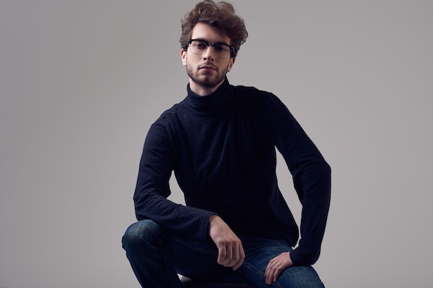 Homem elegante bonito com cabelos cacheados, usando óculos e gola alta preta Foto Premium