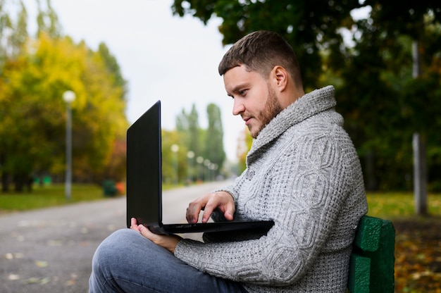Homem em um banco no parque com seu laptop Foto gratuita