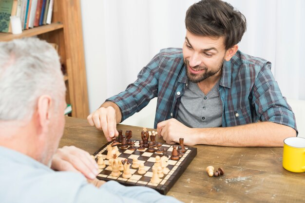 Homem envelhecido e jovem feliz jogando xadrez na mesa no quarto Foto gratuita