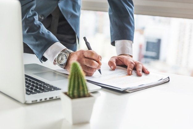 Homem negócios, escrita, ligado, documento, com, caneta, escrivaninha, com, laptop Foto gratuita