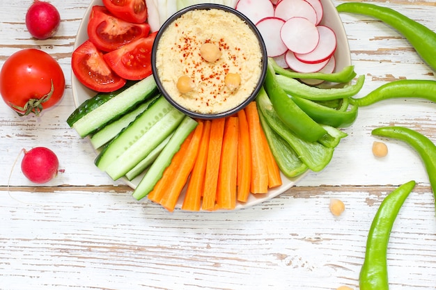 Hummus em tigela, palitos de legumes, grão de bico, azeitonas. | Foto Premium