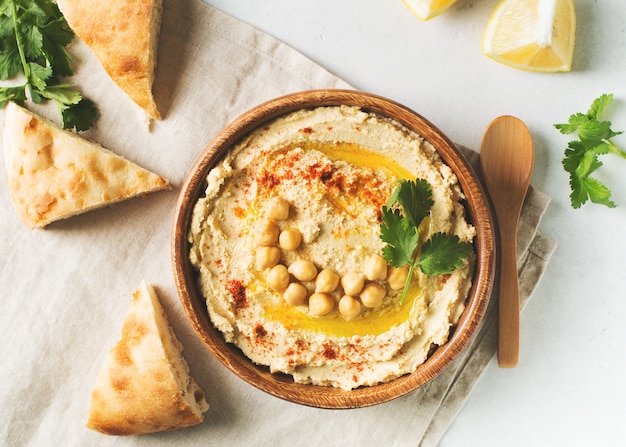 Hummus mergulho com grão de bico, pita e salsa em placa de madeira no fundo branco Foto Premium
