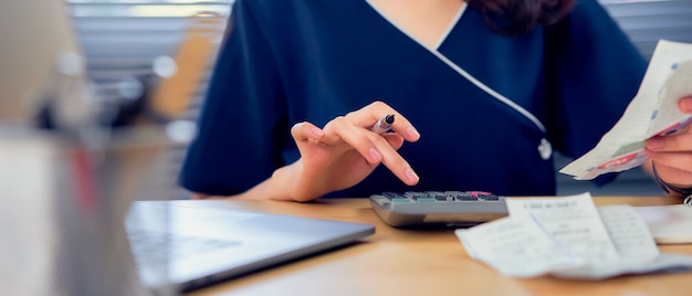 Imprensa de mão de mulher de close-up na calculadora e cálculo mensal de contas de dívida, escrevendo fazer relatório para planejar as despesas no futuro na mesa no escritório em casa. Foto Premium