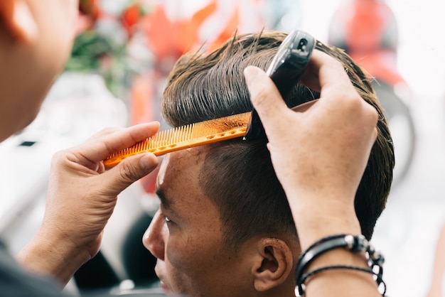 Irreconhecível, cabeleireiro masculino, cortar o cabelo do cliente com aparador e pente Foto gratuita