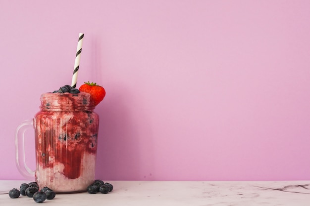 Jar com morango e mirtilos smoothie com palha Foto gratuita