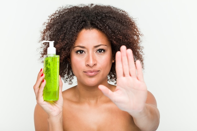 Jovem americana africano segurando a garrafa de aloe vera em pé com a mão estendida, mostrando o sinal de stop, impedindo-o. Foto Premium