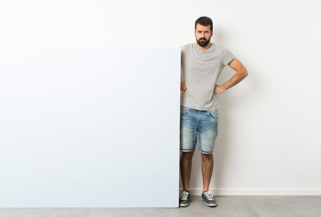 Jovem bonito com barba, segurando um grande cartaz vazio com raiva Foto Premium