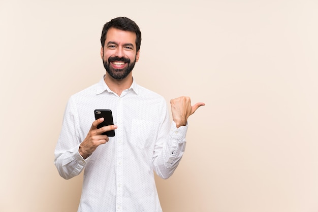 Jovem, com barba, segurando um celular apontando para o lado para apresentar um produto Foto Premium