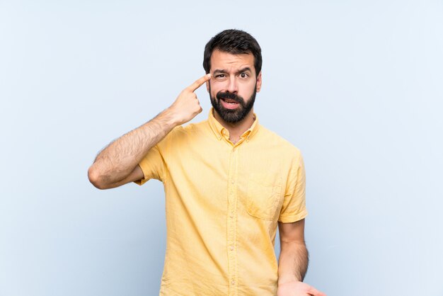 Jovem com barba sobre azul isolado, fazendo o gesto de loucura, colocando o dedo na cabeça Foto Premium