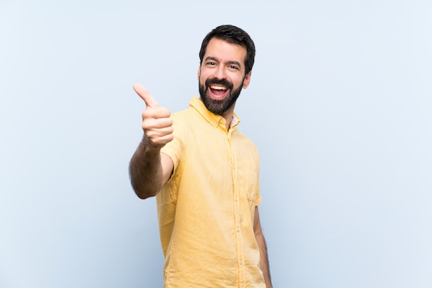 Jovem com barba sobre parede azul isolada com polegares para cima porque algo bom aconteceu Foto Premium