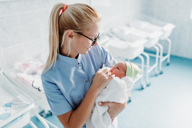 Jovem Enfermeira Em Pé Na Maternidade E Segurando O Bebê Recém Nascido Nos Braços Após O