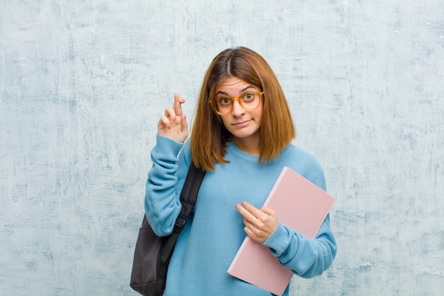 Jovem estudante mulher cruzando os dedos ansiosamente e esperando a boa sorte com um olhar preocupado na parede do grunge Foto Premium