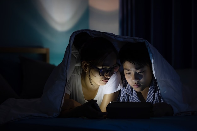 Jovem mãe com filho brincando com um smartphone em uma cama. Foto Premium