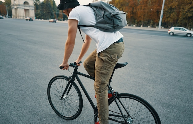 Jovem moderno, andar de bicicleta em uma bicicleta clássica na estrada da cidade com uma mochila Foto gratuita