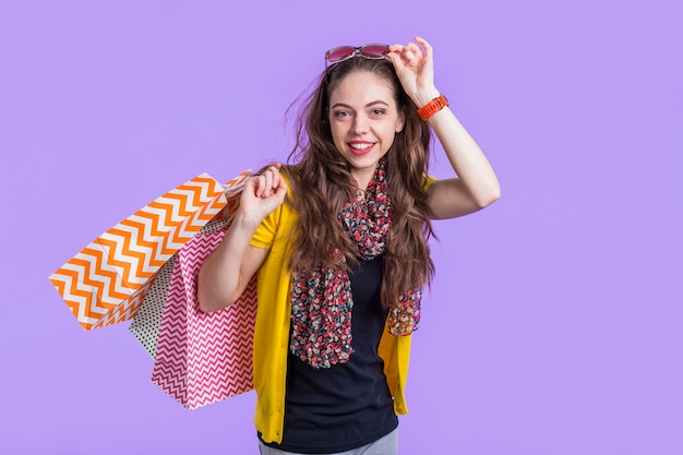 Jovem mulher a sorrir com sacos de compras contra pano de fundo roxo Foto gratuita