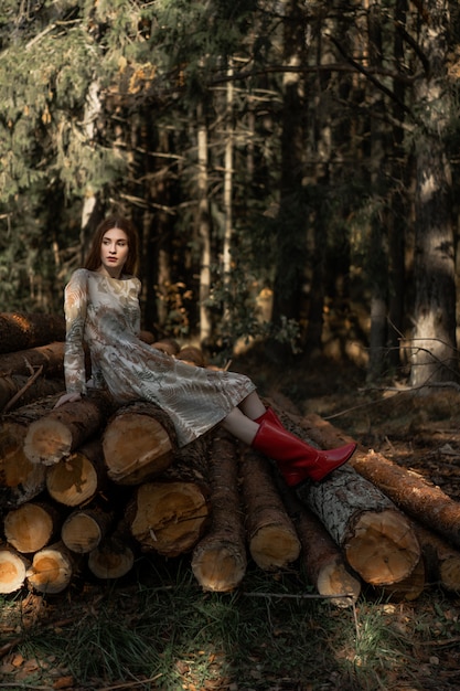 Jovem mulher com longos cabelos ruivos em um vestido de linho recolhendo cogumelos na floresta Foto gratuita