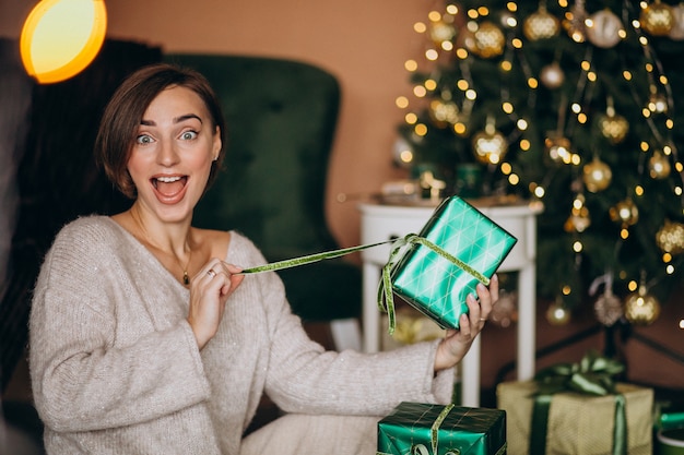 Jovem mulher com presente de natal pela árvore de natal Foto gratuita