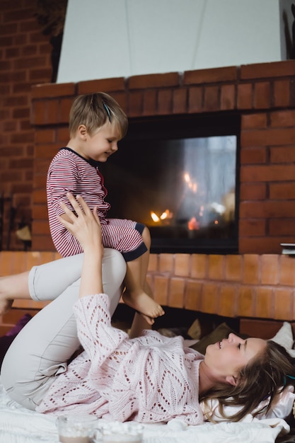 Jovem mulher com uma criança. mãe e filho estão brincando, se divertindo perto da lareira. Foto gratuita