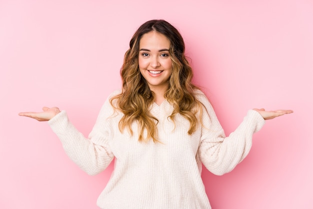 Jovem mulher curvilínea posando em uma parede rosa isolada faz escala