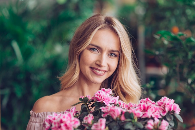 Jovem mulher loura feliz que está atrás das flores cor-de-rosa com fundo borrado Foto gratuita