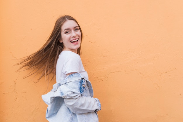 Jovem mulher muito bonita que levanta perto do fundo colorido da parede Foto gratuita