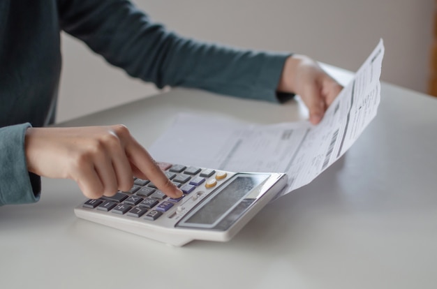 Jovem, mulher, usando a calculadora para análise e cálculo de contas de custo do orçamento familiar relatório na mesa no escritório em casa Foto Premium