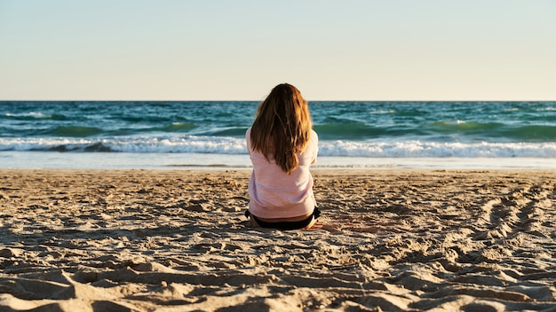 Jovem sentado na areia na praia assistindo o pôr do sol Foto Premium