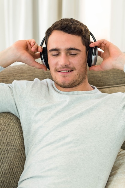 Jovem, sentindo-se relaxado enquanto ouve música com fones de ouvido na sala de estar Foto Premium