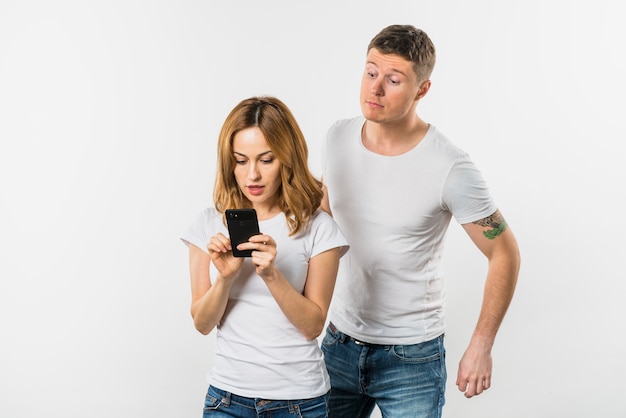 Jovem tentando espionar o celular de uma namorada isolado no fundo branco Foto gratuita