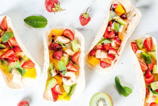 Lanches de verão. comida para uma festa. tacos de frutas com morangos, mangas, bananas, chocolate, menta. em uma mesa de concreto azul claro. copyspace Foto Premium