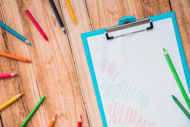 Lápis colorido e prancheta com papel branco na mesa de madeira Foto gratuita