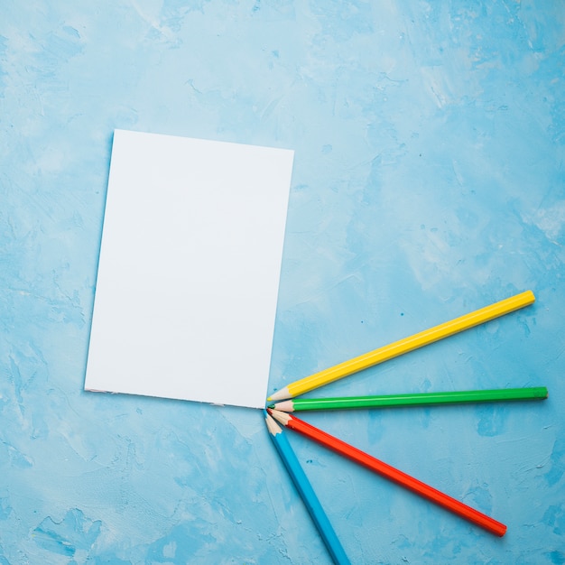 Lápis de cor e folha de papel branco sobre fundo azul Foto gratuita