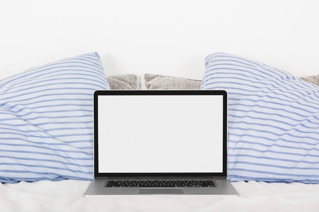 Laptop com tela branca em branco na cama com dois travesseiros Foto gratuita