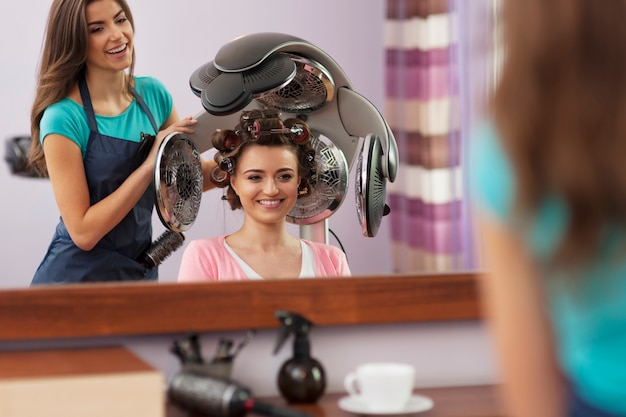 Linda cliente sentada sob o secador de cabelo com rolos Foto gratuita