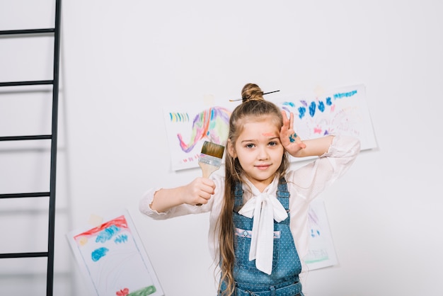 Linda garota de pÃ© com pincel perto de desenhos Foto gratuita
