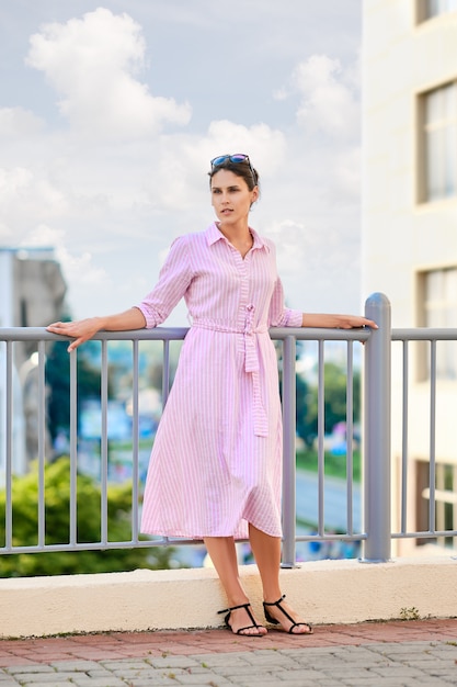 Linda garota de vestido listrado vermelho e óculos de sol em pé na varanda Foto Premium