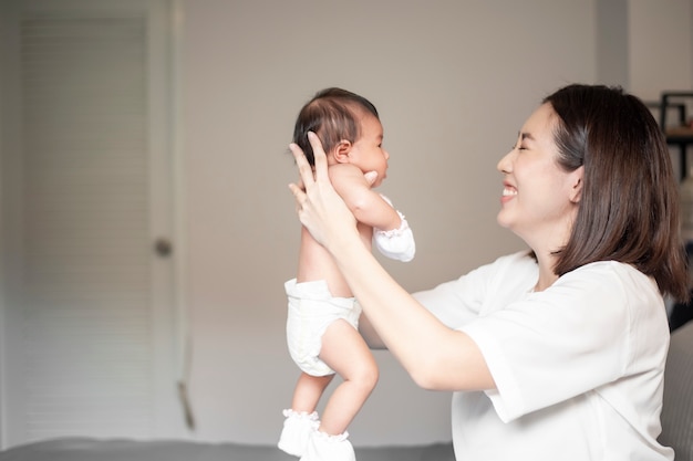 Linda mãe está brincando com seu bebê recém-nascido no quarto. Foto Premium