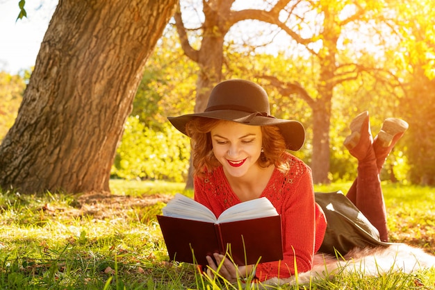 Linda mulher lendo um livro no parque outono sentado na grama | Foto Premium