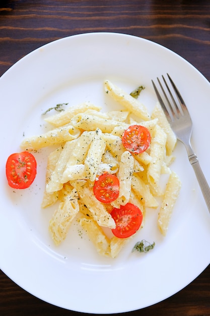 Macarrão com molho de creme, queijo, creme de leite, tomate, ervas e especiarias num prato branco sobre uma mesa de madeira. Foto Premium