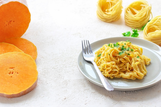 Macarrão de abóbora alfredo fettucine em uma placa de cerâmica com fatias de abóbora crua fresca. outono refeição para o almoço. receita de abóbora. Foto gratuita