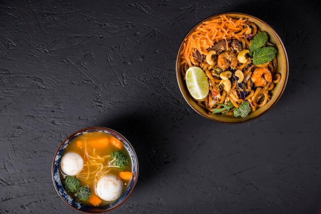 Macarrão udon frito com bola de peixe e sopa de legumes em fundo texturizado concreto preto Foto gratuita
