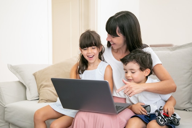 Mãe alegre abraçando crianças felizes enquanto assistiam a um filme ou vídeo no laptop em casa. Foto gratuita