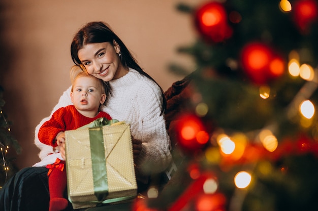 Mãe com filha sentada perto da árvore de natal Foto gratuita