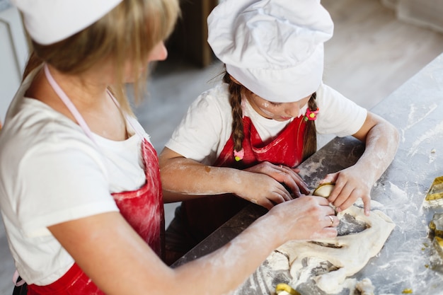 Mãe e filha se divertir preparando biscoitos com leite em uma mesa de jantar na cozinha aconchegante Foto gratuita